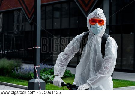 Man Riding Electric Kick Scooter Near Modern Buildings Wearing Anti Covid Protective Suit, Glasses, 