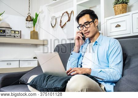 Asian Businessman Is Sitting On The Sofa In His Own House Taking A Call On His Mobile Phone Checking