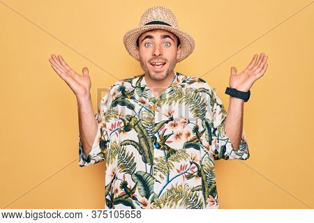 Young handsome man with blue eyes on vacation wearing summer florar shirt and hat celebrating crazy and amazed for success with arms raised and open eyes screaming excited. Winner concept