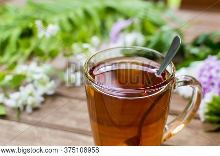 Green Tea Cup With Teaspoon And Floweer Buds On Old Wooden Table, With Copy Space.