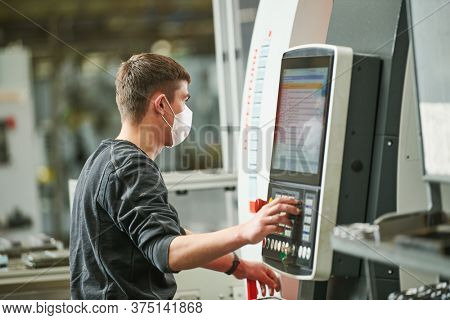 Industrial worker operating cnc machine in protective mask at metal machining industry