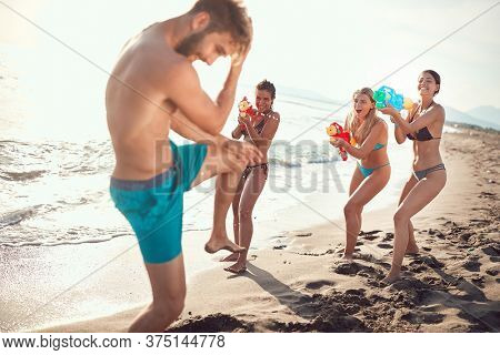 three sexy women sprinkle beardy guy with water guns on sandy beach