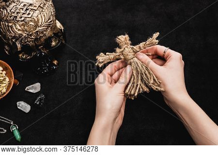 Top View Of Witch Holding Voodoo Doll Near Skull And Crystals On Black