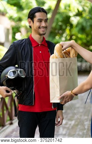 Asian delivery man pick up bakery grocery bag from bakery shop to deliver to customer who make online order. Online food delivery service concept in new normal after coronavirus pandemic.