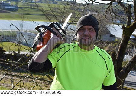 Worker In The Garden With A Chainsaw.