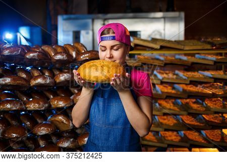 The Stage Of Baking In A Bakery. Portrait Of A Baker Girl With Bread In Her Hands Against The Backgr