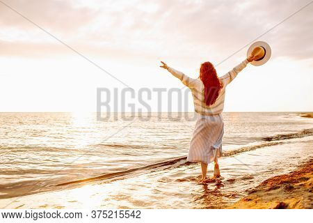 Happy Young Woman In A Dress Holding Straw Hat And Walking Alone On Empty Sand Beach At Sunset Sea S