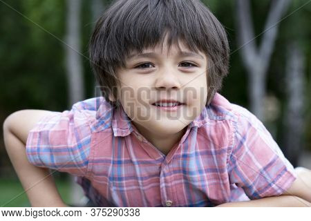 Healthy Kid Relaxing In The Park With Blurry Natural Bokeh Background, Cute Little Boy Looking At Ca