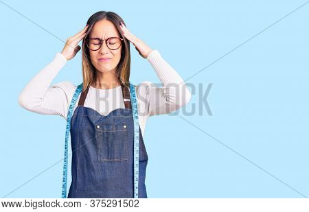 Beautiful brunette young woman dressmaker designer wearing atelier apron suffering from headache desperate and stressed because pain and migraine. hands on head. 