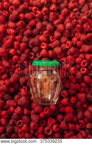Empty Glass Jar For Raspberry Cooking, On The Texture Of Red Ripe Raspberry In The Background.