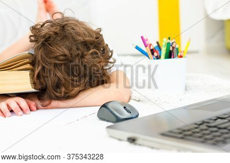 Tired Little Boy Sitting And Doing Homework, With Hishead On His Arm Near His Notebook While . Conce