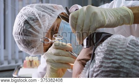 Suturing stitches. Oral surgeon performing surgery installing implant into senior woman mouth. Dentist works with a patient in modern dental clinic