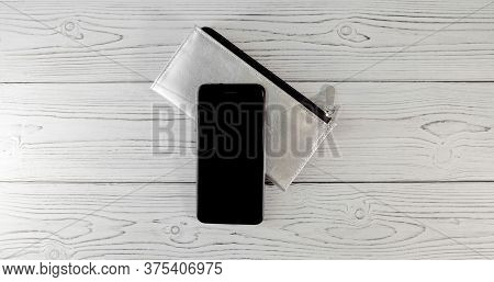 Silver Wallet With Black Clasp And An Expensive Black Smartphone With Two Cameras On A Wooden Board 