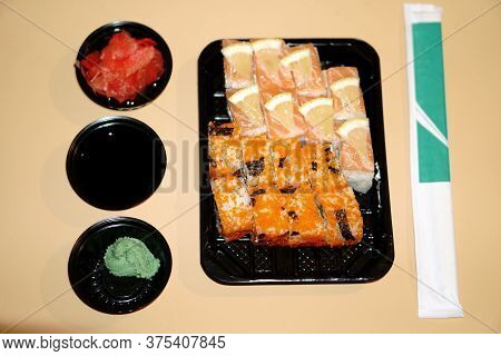 A Set Of Sushi Rolls In A Plastic Container And Additional Spices In A Plastic Bowl
