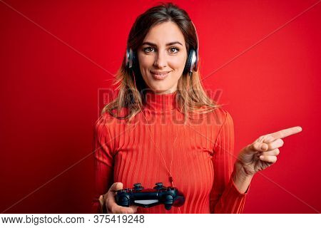 Young beautiful brunette gamer woman playing video game using joystic and headphones very happy pointing with hand and finger to the side