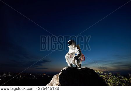 Brave Spaceman Hunkering Down On Top Of Mountain With Mesmerizing Blue Sky On Background. Cosmonaut 