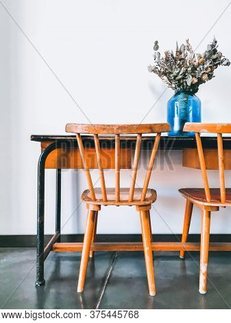 Vintage Wooden Elementary School Desk And Two Wooden Chairs With A Dried Flower Arrangement In A Blu