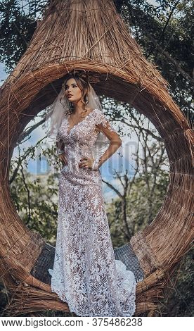 Beautiful Bride In Her Wedding Dress Posing For Photos On A Wooden Swing In The Tree.