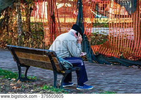 Back View Of An Old Man Standing On Bench In Park In Talking On His Phone In Lugoj, Romania, 2020