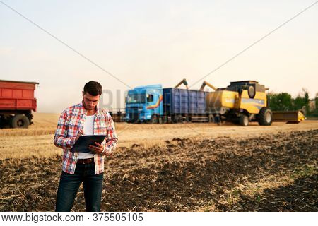 Farmer Controls Loading Wheat From Harvester To Grain Truck. Driver Holding Clipboard, Keeping Notes