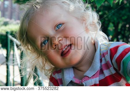 Portrait Of A Cute Happy Little Boy With Blond Hair And Blue Eyes, Whearing A Hat, Smiling And Playi