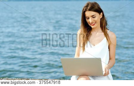 Smiling Girl With Laptop On Her Lap Sits On A Dock Not The Shore Of The Ocean Lake