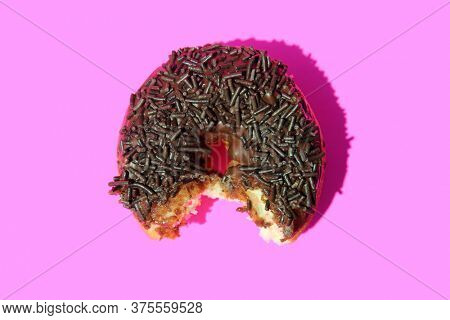 Donut. Cake Donut with Chocolate Frosting and Chocolate Sprinkles. Donut with bite taken out on a pink background.