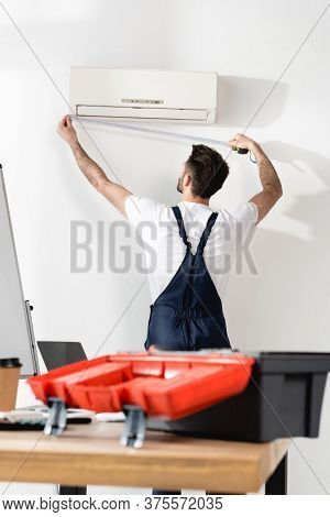 Selectiive Focus Of Repairman Measuring Air Conditioner Near Office Desk With Toolbox