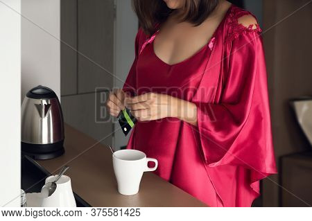 Woman Making Morning Tea To Have With Breakfast At Home, A Girl In A Satin Nightgown And Red Robe Ma