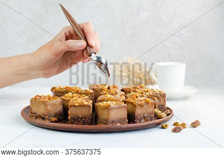 Chocolate Syrup Dripping From A Spoon In Hands For A Raw Vegan Dessert. Cakes With Pistachios, Peanu