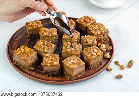 Chocolate Syrup Dripping From A Spoon In Hands For A Raw Vegan Dessert. Cakes With Pistachios, Peanu