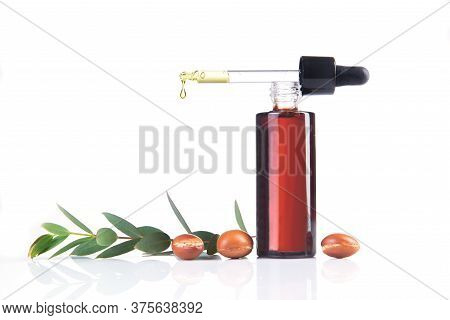 Bottle Of Argan Oil With Fresh Leaves And Fruits On A White Background. Drop Of Oil Pourig From The 