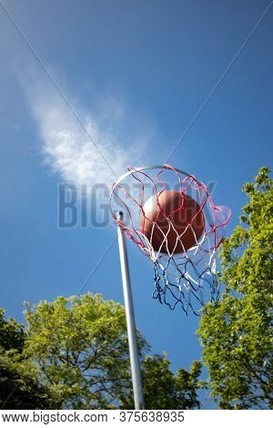 Looking Up At Netball In Mid-air In The Netball Goal With A Cloud Trail Following Against A Clear Bl