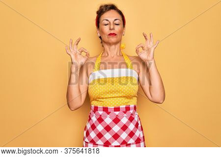 Middle age senior pin up housewife woman wearing 50s style retro dress and apron relax and smiling with eyes closed doing meditation gesture with fingers. Yoga concept.