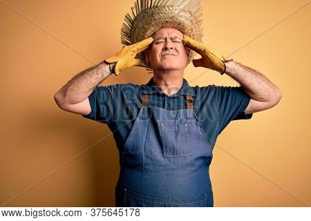 Middle age hoary farmer man wearing apron and hat over isolated yellow background suffering from headache desperate and stressed because pain and migraine. Hands on head.