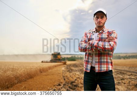 Happy Farmer Proudly Standing In A Field With Arms Crossed On Chest. Combine Harvester Crop Rich Whe