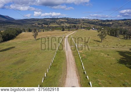 Aerial View Of A Dirt Road With White Fence Post Markers In A Green Agricultural Field
