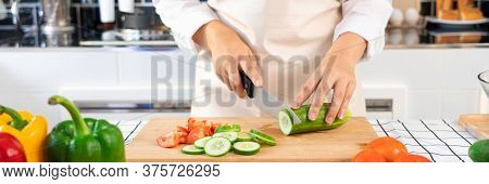 Young Asian Woman Is Preparing Healthy Food Vegetable Salad By Cutting Cucumber For Ingredients On C