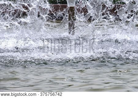 Selective Focus On Spray Of Urban Fountain And Blurred Background. A Fountain With Splashes And Drop