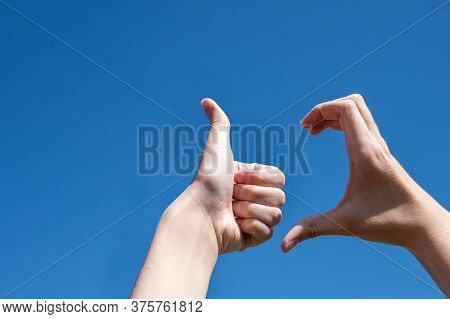 Close-up Of Two Hands Making A Thumb Up Sign, Half Heart On A Blue Background, Copy Space. Friendzon