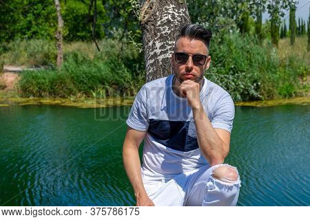 Young Man In White Pants And Modern Styling Posing In The Freshwater Pond Of Clot De La Mare De Deu 