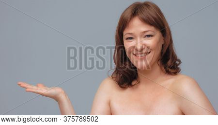 Cherfull Mature Woman Opens Palm Showing Empty Space For Text Or Promotional Items. Smiling Pretty W