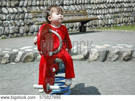 Beautiful Baby Asian Girl Playing With Toy Horse Outdoors In Public Park.