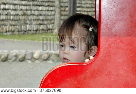 Beautiful Baby Asian Girl Outdoors In Public Park With Thoughtful Look. Defocused Background With St