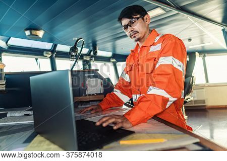Filipino Deck Officer On Bridge Of Vessel Or Ship. He Is Using Laptop, Electronic Paperwork At Sea