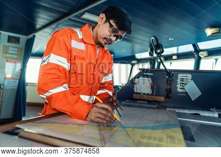 Filipino Deck Officer On Bridge Of Vessel Or Ship. He Is Plotting Position On Chart