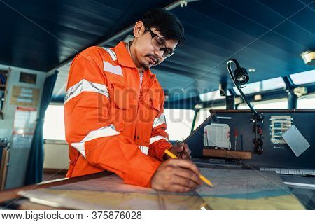 Filipino Deck Officer On Bridge Of Vessel Or Ship. He Is Plotting Position On Chart