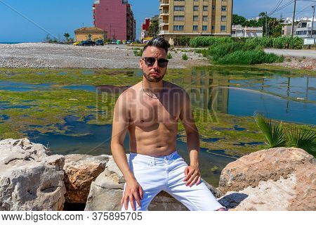 Young Man In White Pants And Modern Styling Posing In The Freshwater Pond Of Clot De La Mare De Deu 