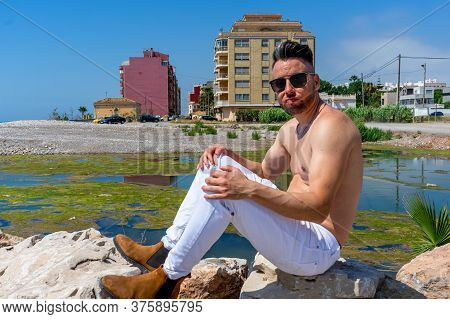 Young Man In White Pants And Modern Styling Posing In The Freshwater Pond Of Clot De La Mare De Deu 