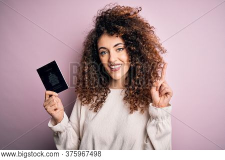Beautiful tourist woman with curly hair and piercing holding canada canadian passport id surprised with an idea or question pointing finger with happy face, number one